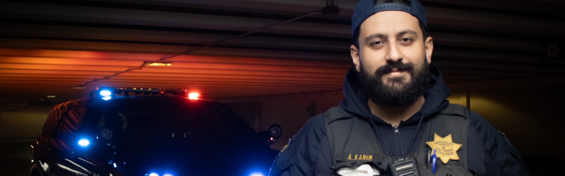 Image of UPD officer standing in front of UPD Police SUV with lights on