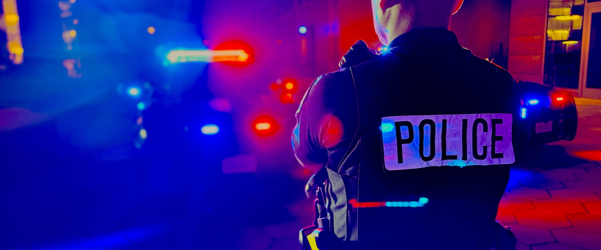 Image of a police officer standing in front of a police vehicle with lights on